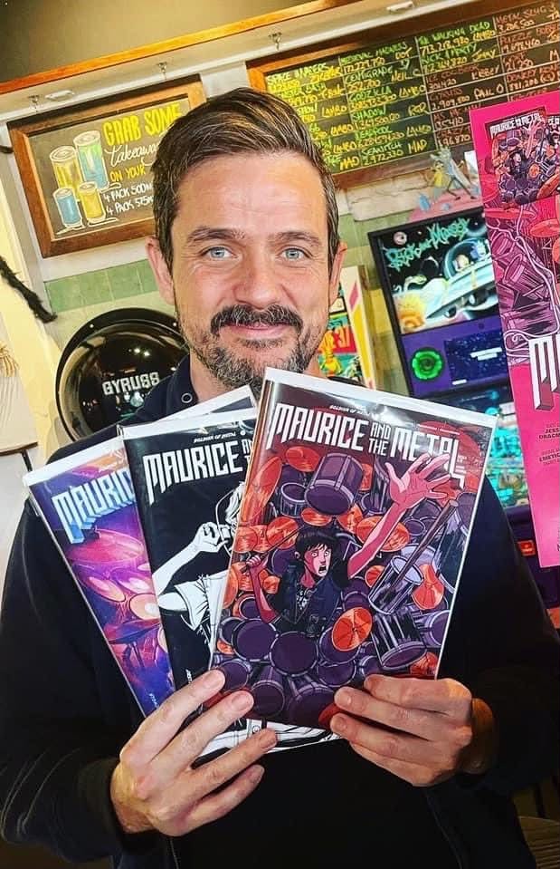 Aaron Sammut holding issues of the Maurice & The Metal comic